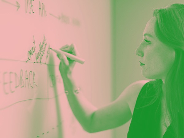 Photo in green tone with a woman writing with a pen on a white board.