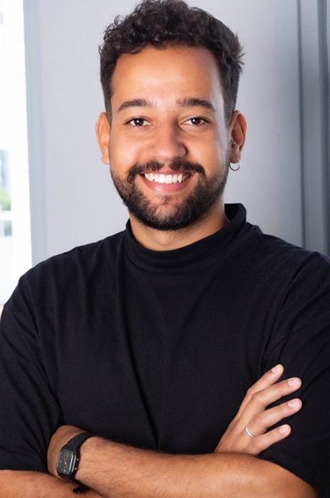 Photo of Denilson, who has brown skin, short dark hair, looking straight ahead and smiling.