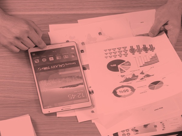 Photo of a person with a cell phone and papers with graphs on a table.