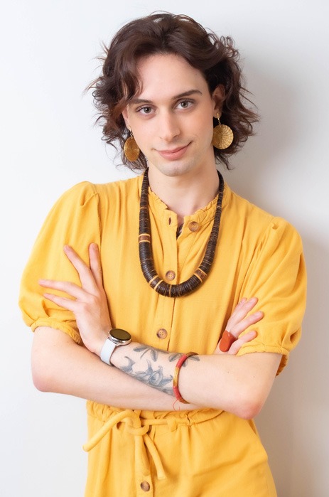 Photo of Vinicius, white skin, short hair, wears a yellow shirt, necklace and has his arms crossed