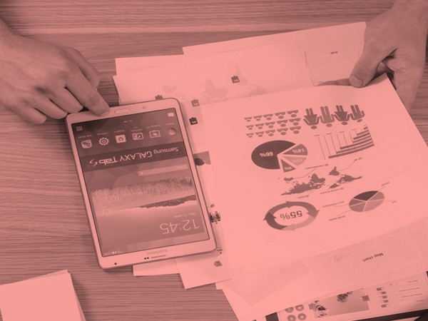 Foto de pessoa com celular e papéis com gráficos em uma mesa.