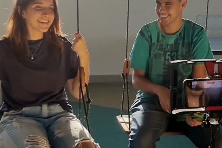 uma mulher e um homem sentados em um balanço, ambos sorrindo e olhando para a gravação